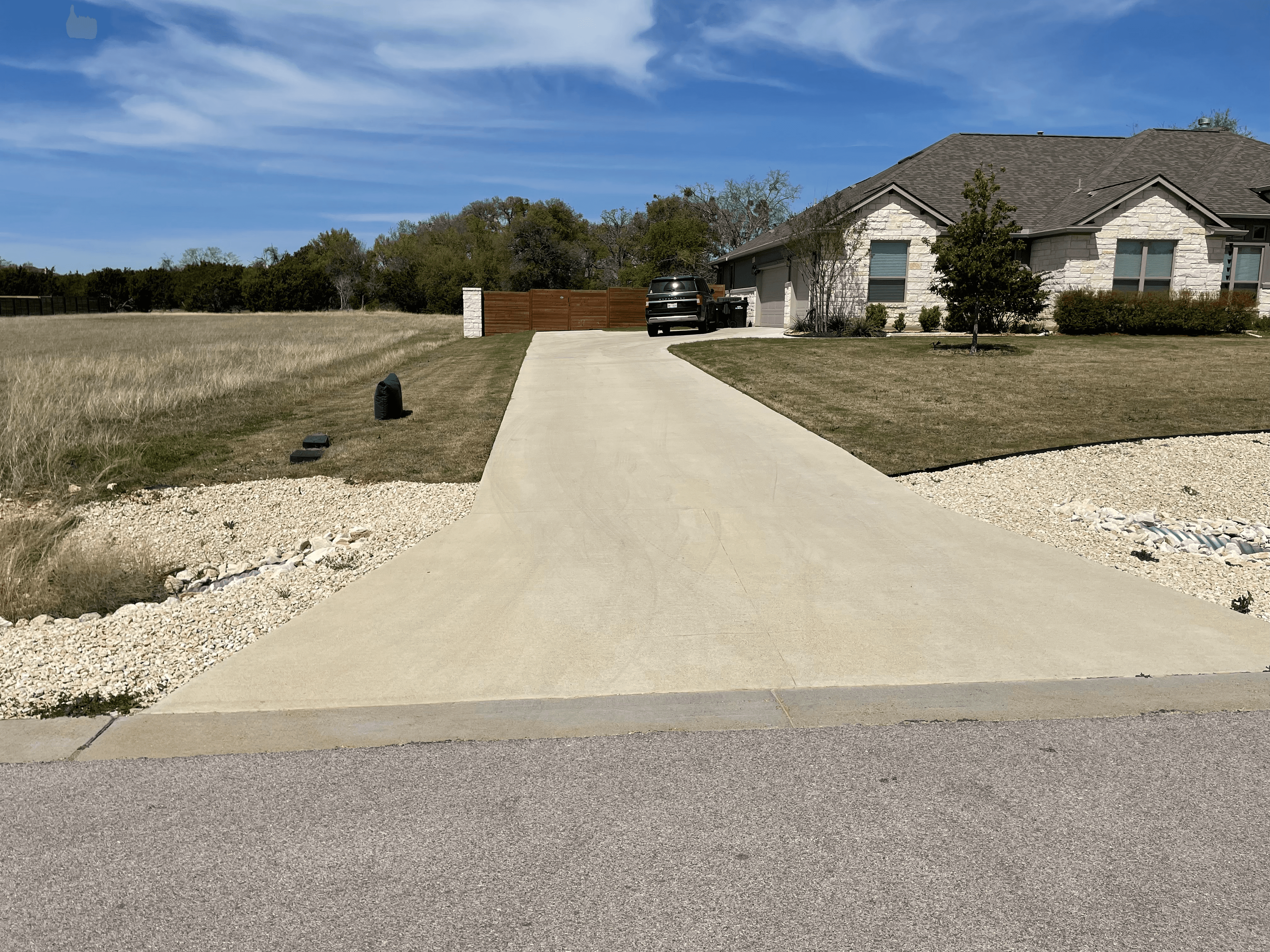 Long concrete driveway leading to a stone house with a black SUV parked outside.