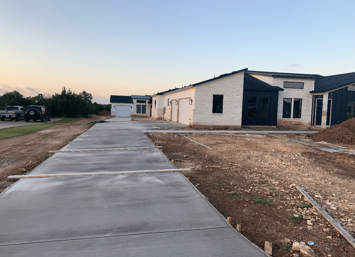 Freshly poured concrete driveway leading to a modern white stone house with black accents.