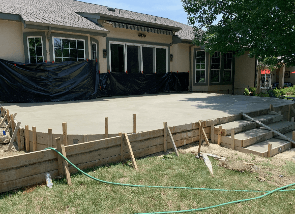 Newly poured concrete patio and steps with wooden forms in a residential backyard setting.